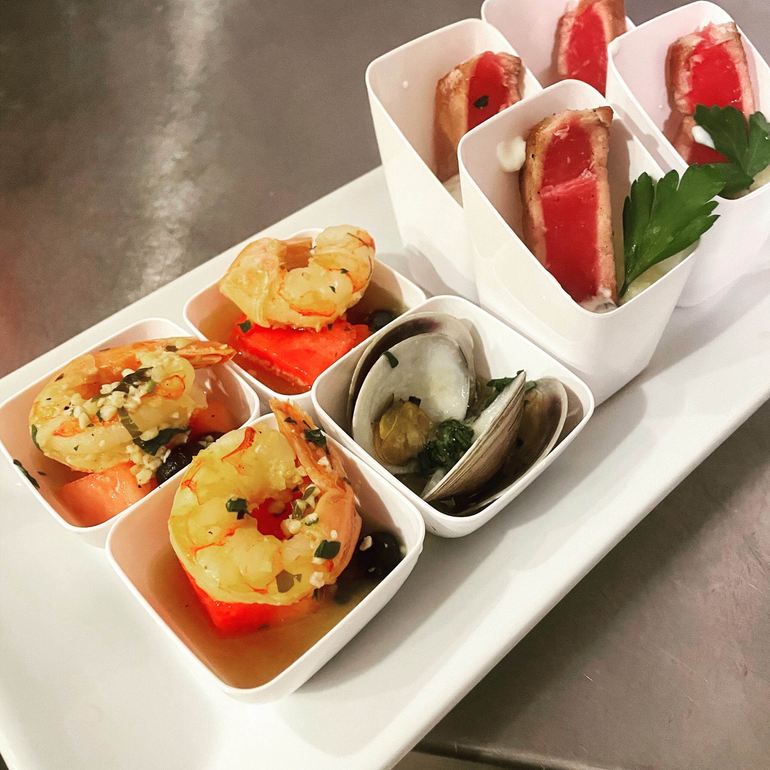 Seafood appetizer selection with shrimp, clams, and seared tuna in white tasting bowls