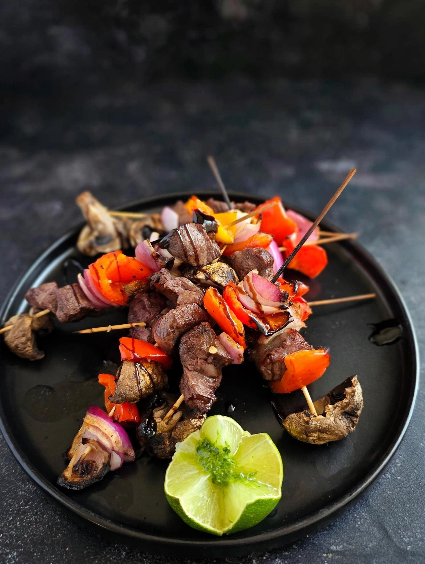 Grilled meat and vegetable kebabs on a black plate for a wedding or special event menu