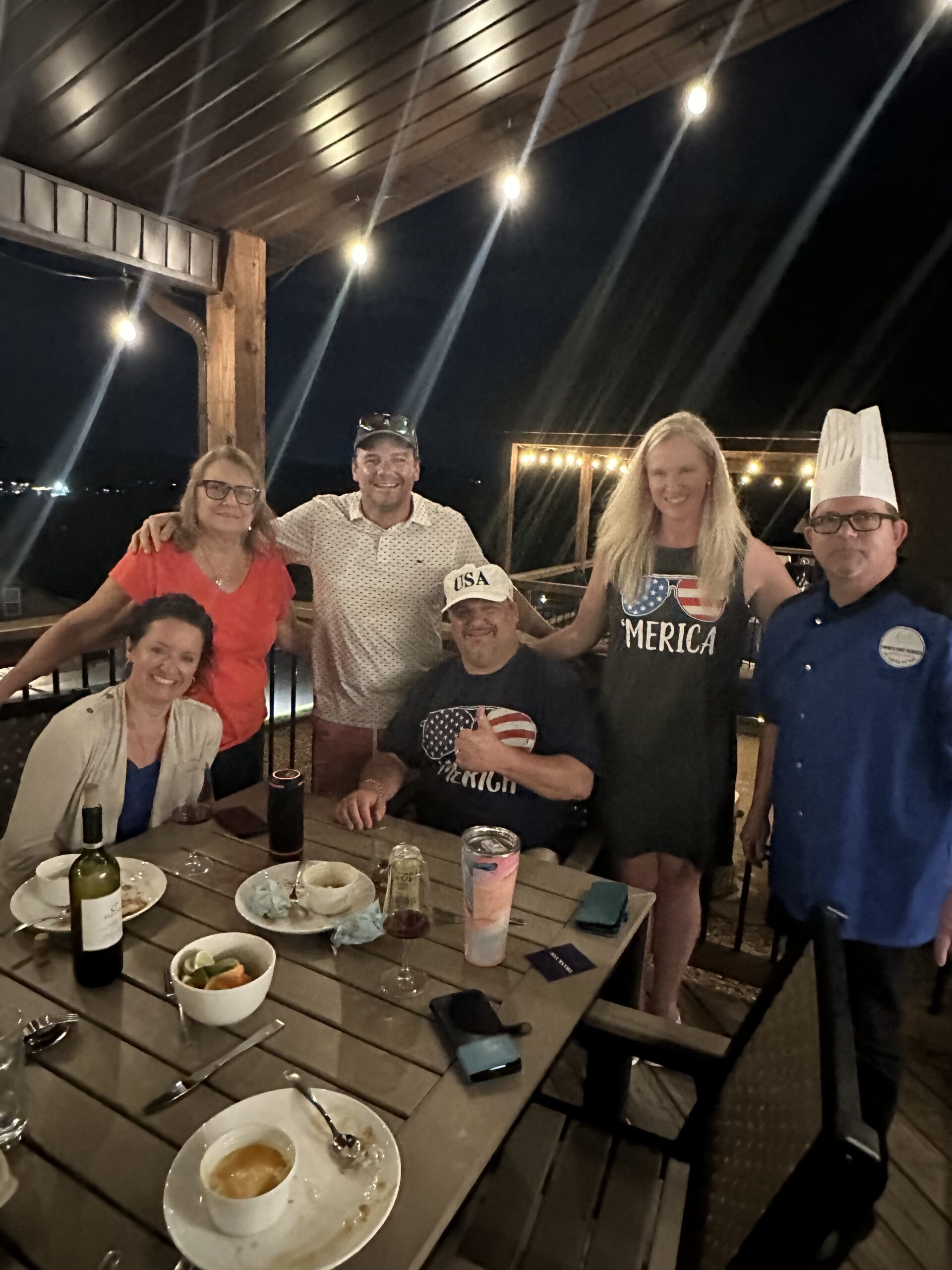 Group dining photo at an evening event with guests gathered around a table outdoors