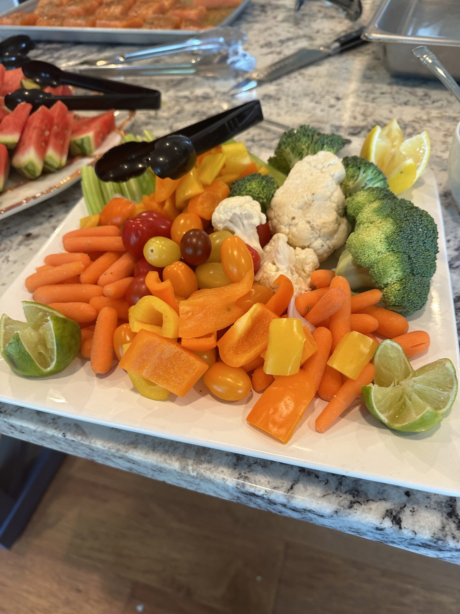 Vegetable tray with broccoli, cauliflower, carrots, bell peppers, cherry tomatoes, and lime wedges for a wedding or special event menu